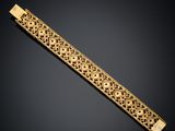 a gold bracelet with an intricate design on a black background