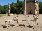 trois chaises et une table devant un bâtiment sur lequel se trouve une horloge