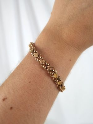 someone is holding a gold bracelet with a flower design on it