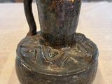 un vase marron posé sur une table, avec un mur en pierre en arrière-plan