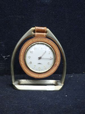 une petite horloge posée sur un socle, sur une surface noire