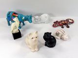 Plusieurs figurines représentant des chats et des éléphants sont posées sur une surface blanche