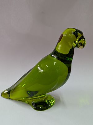 un oiseau en verre vert posé sur une surface blanche