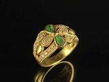 a gold ring with green stones and diamonds on a black surface