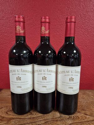 three bottles of wine sit on a wooden table in front of a red wall