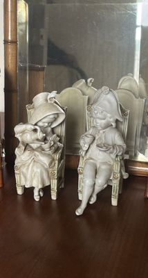 deux figurines représentant des enfants assis sur une chaise devant un miroir