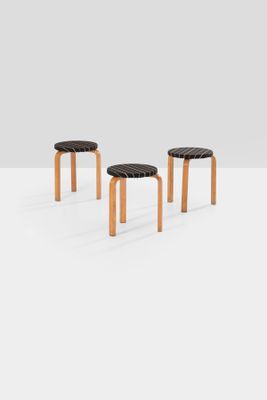 three wooden stools with black leather seats on a white surface