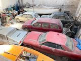 several old cars are parked in a garage with a boat in the background