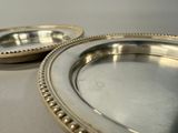 two silver plates with beaded edges sitting on a table