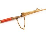 une image représentant un stylo rouge et doré muni d'une chaîne, sur fond blanc