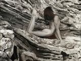 a nude woman sitting on a rock with her legs crossed
