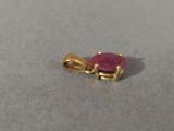 yellow gold pendant with a pink stone on a gray surface