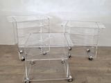 trois tables d'appoint en acrylique transparent équipées de roulettes, posées sur un parquet