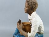 a figurine of a boy sitting on the ground holding a bowl