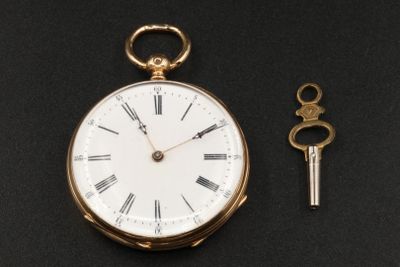 une montre de poche en or et une clé posées sur une surface noire
