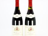 two bottles of red wine sitting next to each other on a white surface