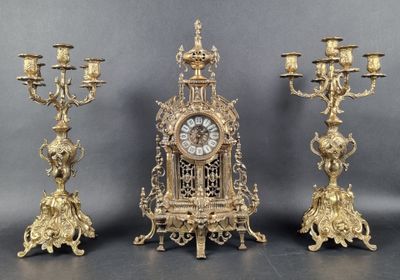 three gold colored candlesticks and a clock on a table