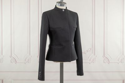 the black jacket is on a mannequin stand in front of a white wall