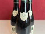 three bottles of wine sitting on a table in front of a red wall