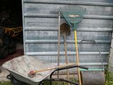 a wheelbarrow, rake and a wheelbarrow in front of a garage