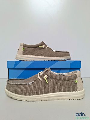des chaussures pour homme dans une boîte posée sur une surface blanche, avec une boîte bleue en arrière-plan