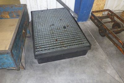 une grille métallique posée au sol, à côté d'un chariot en bois
