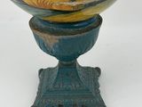 a yellow and blue vase on a stand on a white surface