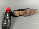 pair of black leather shoes with red soles on a grey surface