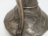 a silver vase with a handle on a white surface