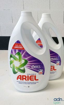 trois flacons de lessive liquide Ariel posés sur un plan de travail à côté d'un flacon de lessive en poudre