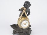 a small statue of a boy holding a clock on a branch