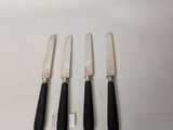 four black handled knives sitting next to each other on a white surface
