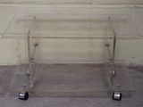 une table en verre transparent munie de roulettes, posée sur un sol en béton