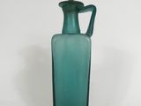 a green glass bottle with a handle on a white surface