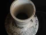 un vase blanc orné d'un motif, posé sur une surface noire
