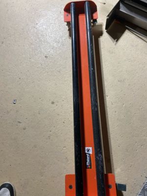 an orange pipe cutter sitting on top of a floor next to a pair of shoes