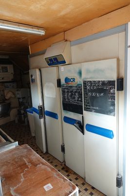 Plusieurs réfrigérateurs sont alignés dans une cuisine où se trouve un tableau noir accroché au mur.