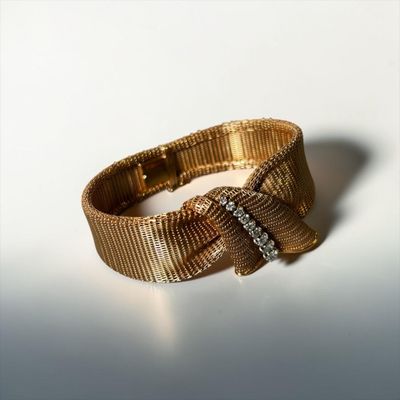 a close up of a gold bracelet with a bow on it