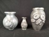 three silver vases sitting next to each other on a black background