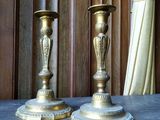 une paire de bougeoirs anciens en laiton posés sur une table devant un rideau