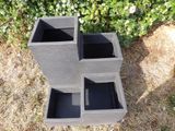 a black planter sitting on the ground next to a bush