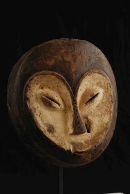 un masque en bois posé sur un socle, sur fond noir