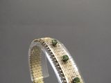 un gros plan sur un bracelet en or orné de pierres vertes