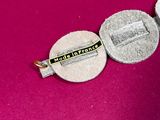 a silver coin with a pin on it sitting on a pink surface