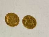 two pieces of gold coins sitting on top of a white surface