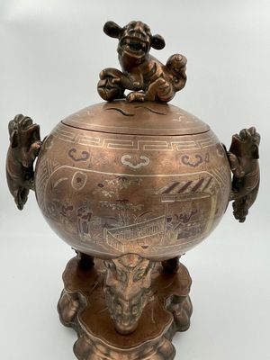 un vieux vase en bronze surmonté d'un singe assis