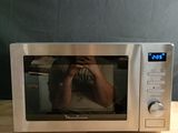 une personne en train de se prendre en photo dans un micro-ondes posé sur une table en bois