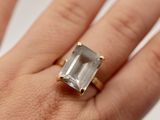 une image représentant la main d'une femme tenant une bague sertie d'une émeraude