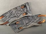 two pieces of denim with leather straps on a gray surface