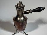 a silver coffee pot with a black handle on a white table